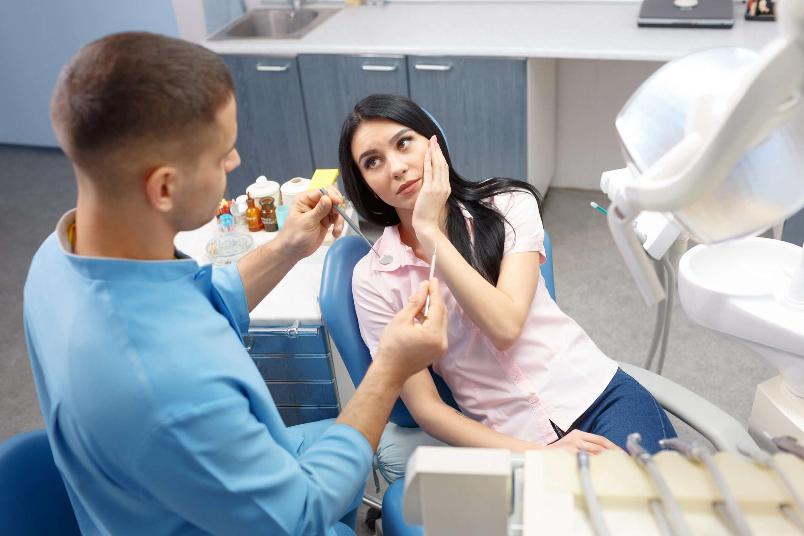 A concerned patient holding her jaw consults with a dentist in a clinical setting, potentially discussing how long wisdom teeth swelling lasts and steps for recovery.