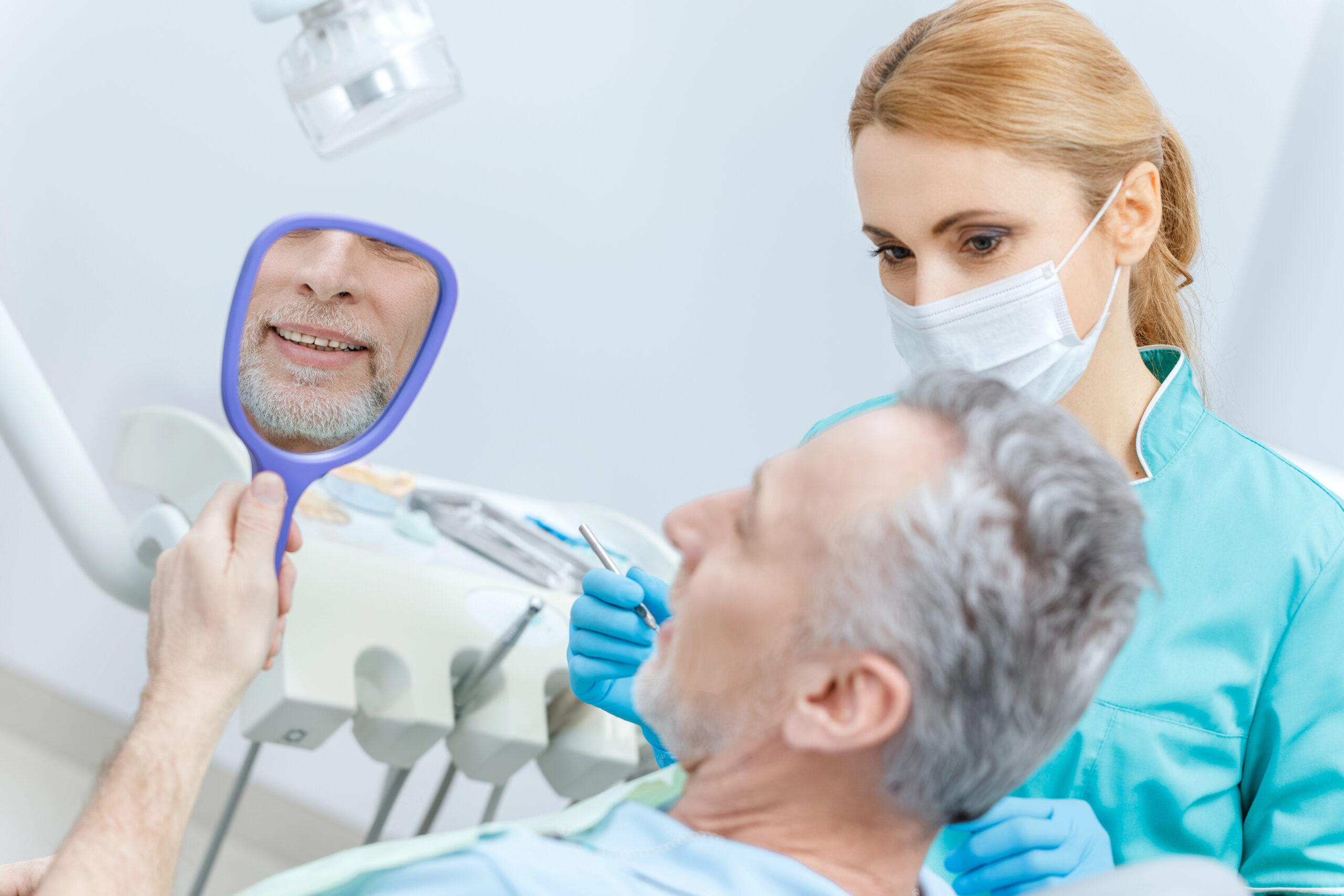 A patient examines his smile in a hand-held mirror while the dentist observes, possibly discussing treatment or recovery steps for pericoronitis after wisdom teeth removal.