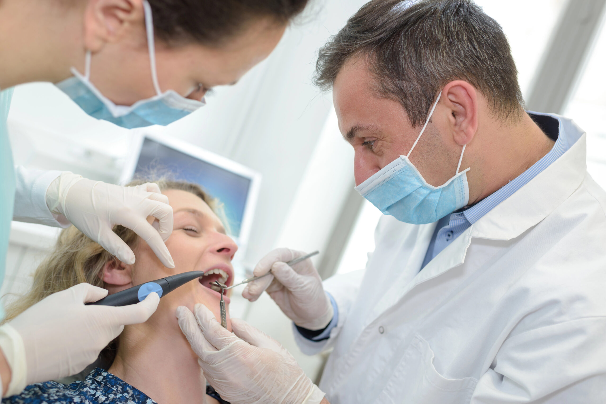 A dentist and an assistant are performing a dental procedure on a patient using specialized tools in a clinical setting, which could involve wisdom teeth removal.