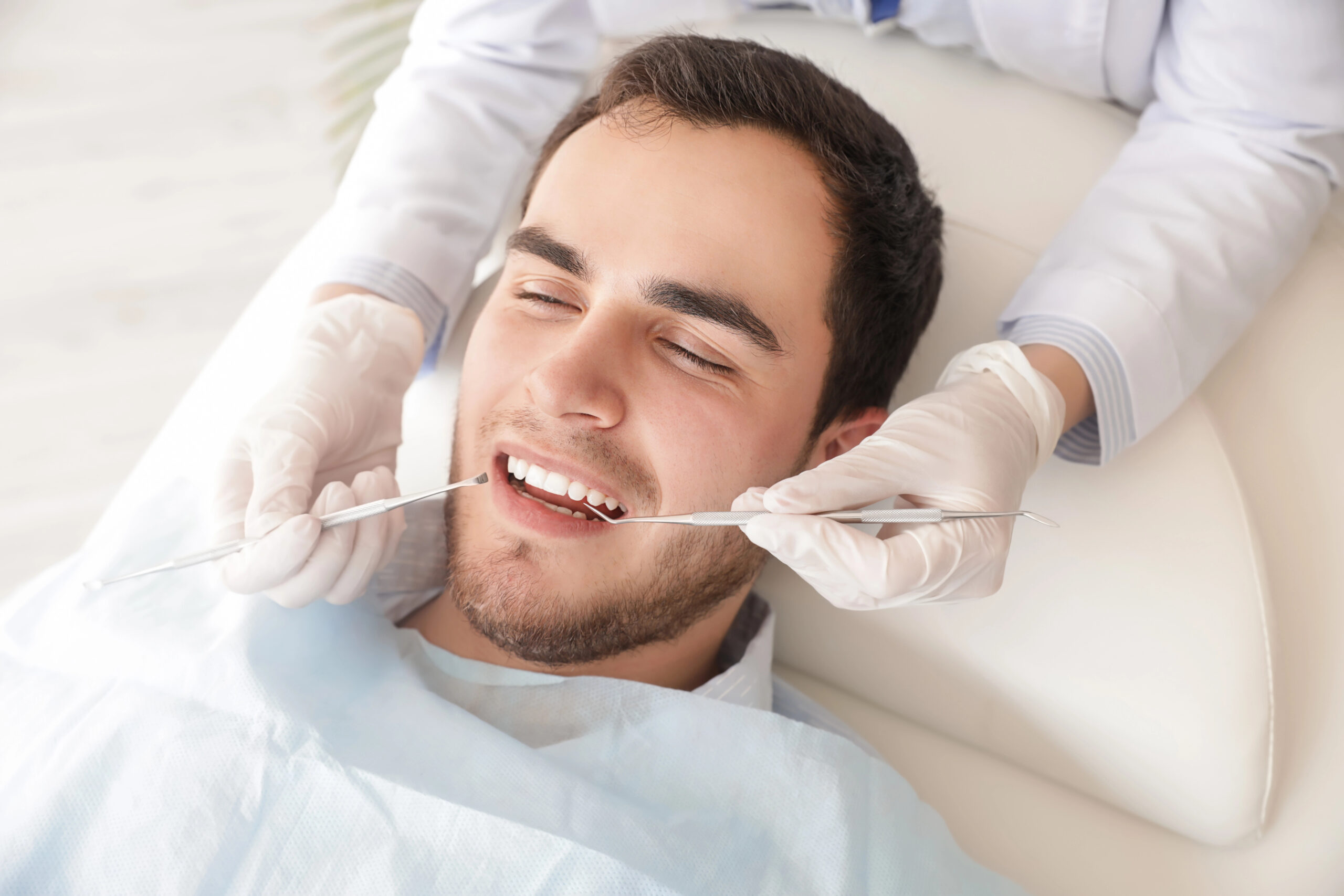 A smiling patient undergoes a dental check-up, raising the question, "can you drive after wisdom teeth removal," which depends on the type of anesthesia used during the procedure.