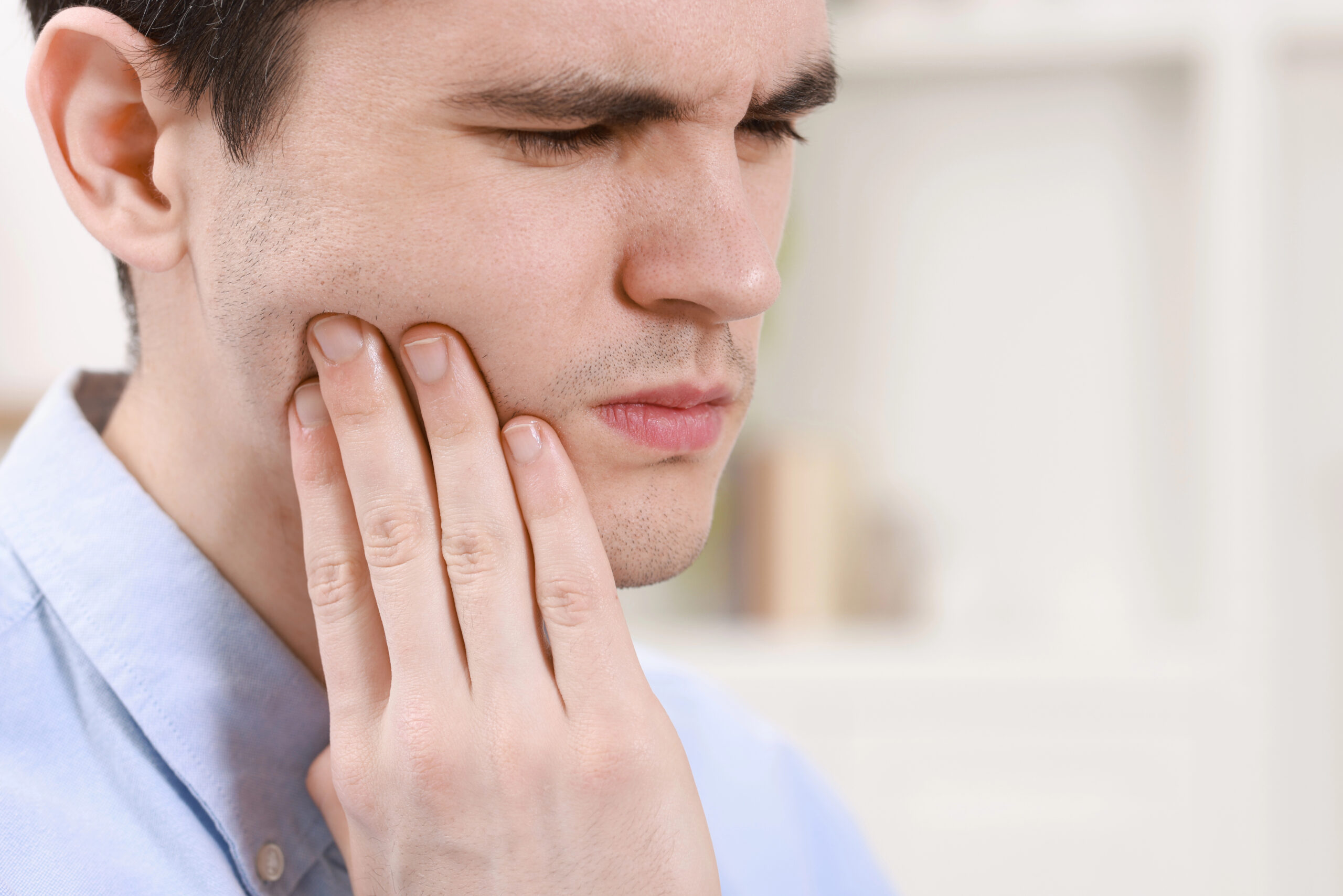 A man holds his jaw in discomfort, illustrating the common issue of jaw pain after wisdom tooth extraction and the need for proper post-operative care.